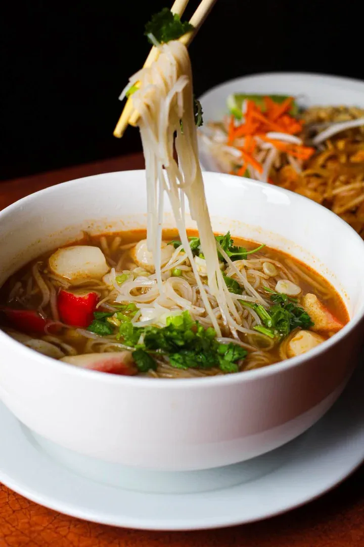 Rice noodles lifted with chopsticks from a bowl of noodle soup