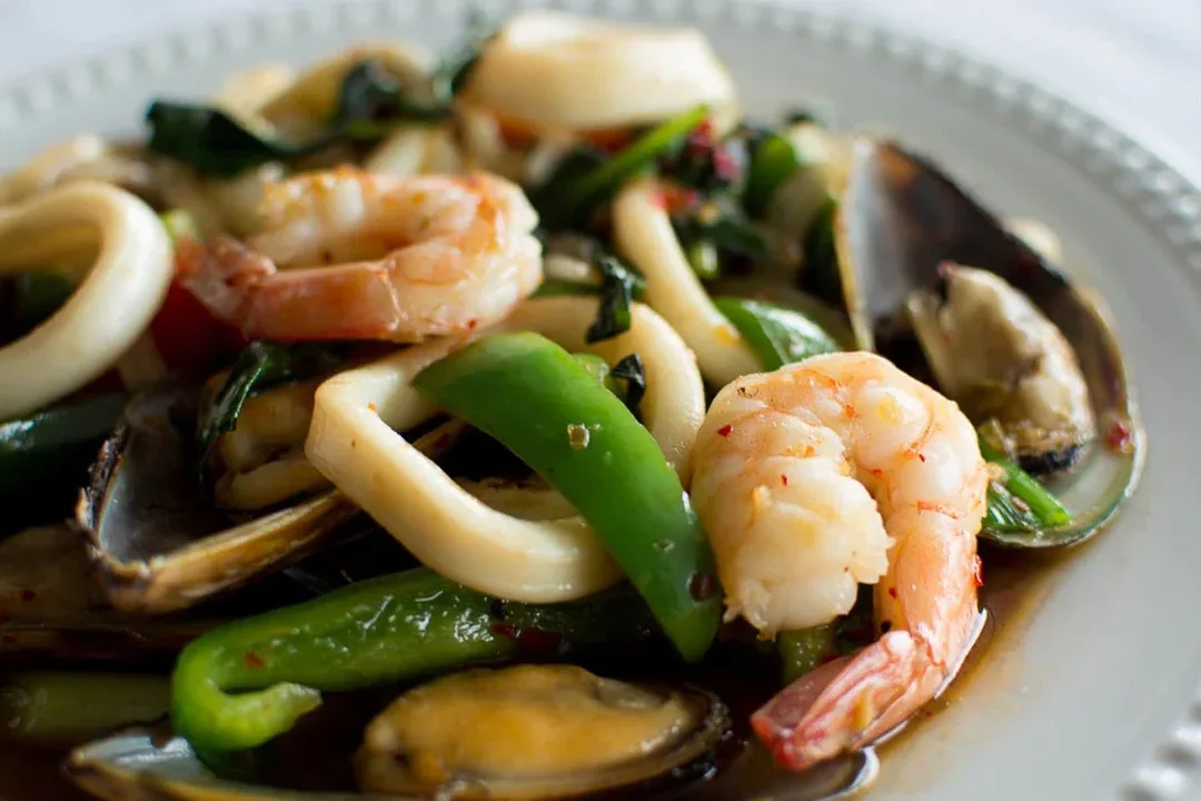 Shrimp, squid and mussels stir-fried with green pepper on a white plate