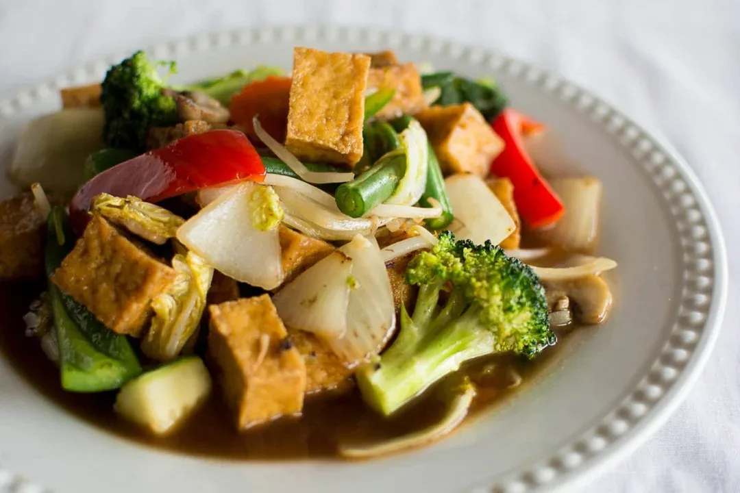Tofu and vegetable stir-fry with broccoli and red pepper on a white plate